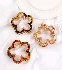 Macro shot of three flower-shaped claw clips with tortoise patterns on white silk fabric