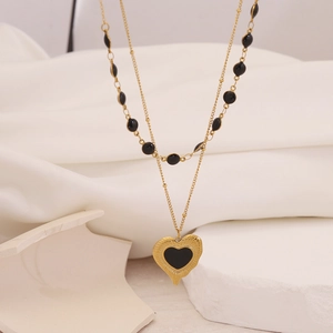 Detail of layered gold necklace featuring black beads and a black enamel heart pendant