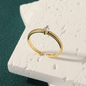 Minimalist gold textured open ring with small round zircon on white stone background