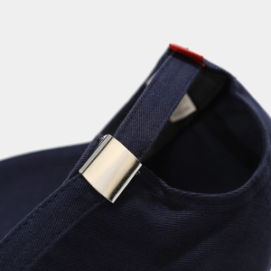 Detail of navy blue cotton baseball cap featuring silver metal buckle and red woven label