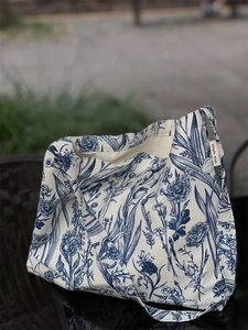 Detail of blue floral plant pattern on a beige canvas tote bag with side brand label