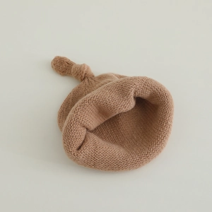 Détail du bonnet en tricot pour bébé en couleur chameau avec un nœud sur le dessus