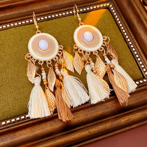 Detail of vintage bohemian earrings with white faux stones, gold leaves and soft tassels