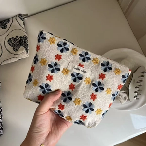 Detail of hand-held small canvas makeup bag with colorful floral embroidery and label