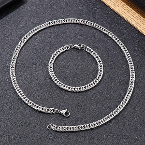 Flat lay of silver curb chain necklace and bracelet set on black textured background