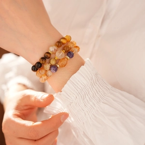 Close-up of stacked tiger eye, amethyst, and citrine bead bracelets with gold accents