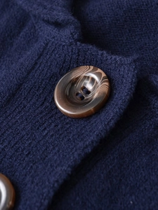 Makro-Detail von dunkelblauem Strickpullover mit Textur und braunem Knopf in Marmoroptik