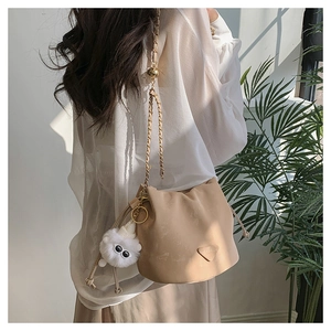 Detail of beige chain bucket bag with plush charm and FASHION lettering on model
