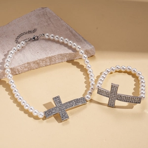 Baroque pearl necklace with rhinestone-encrusted cross pendant on textured stone background