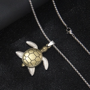 Vintage sea turtle pendant necklace in silver and bronze tones on a black background