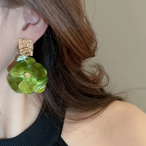 Detail of green acrylic flower earring with hammered gold metal texture on ear