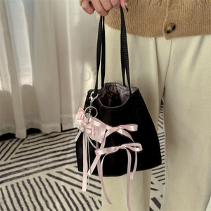 Close-up of black velvet ballet-style handbag with pink ribbon bows and pearl charms