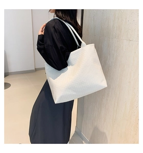 Detail shot of a white woven oversized tote bag showing texture and capacity on a shoulder