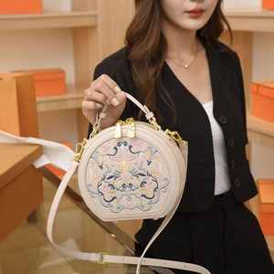 Close-up of ethnic floral embroidery and gold hardware on a beige round crossbody bag