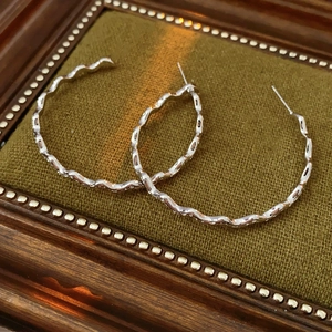 Detailed view of silver wavy C-shaped hoop earrings on green velvet background