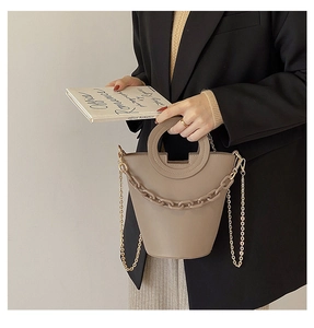 Detail of khaki bucket bag featuring a resin chain and metallic strap on black blazer