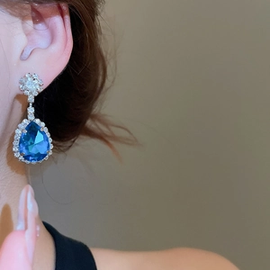 Close-up of elegant blue teardrop dangle earrings with sparkling stones on a model