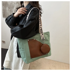 Detail of light green canvas tote bag with brown pocket and patterned strap on model