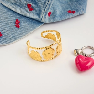 Detail of a gold floral镂空 cuff bracelet with flower design on blue denim background