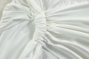 Detail of white knit fabric showing twisted ruching and elastic texture on a dress