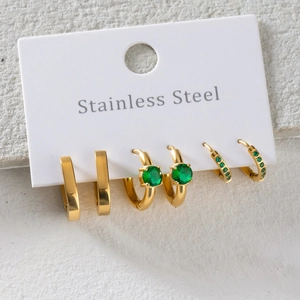 Three pairs of gold stainless steel earrings with green zircon stones on stone background