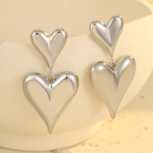 Orecchini a doppio cuore in acciaio inossidabile argento lucido su sfondo ceramico bianco