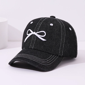 Detail showing white bow embroidery on black denim baseball cap with contrast stitching