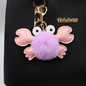 Cute purple plush crab keychain with pink leather claws and gold metal clasp on a bag