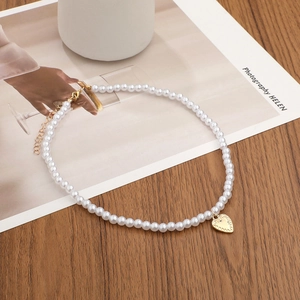 Elegant white faux pearl necklace with gold heart pendant on a rustic wooden surface