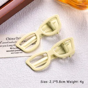 Detail of two cream-colored sunglasses-shaped hair clips with matte finish, size 2.1x5.8cm
