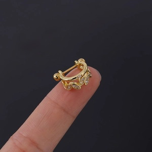 Detail of a tiny gold-plated crown earring with white zircon inlay held on fingertips