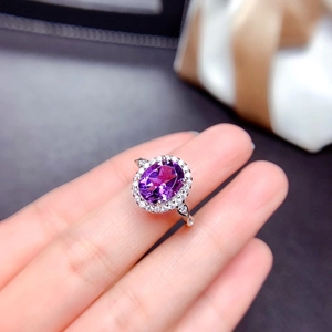 Close-up of a silver ring with a large oval purple amethyst and white stone halo on a finger
