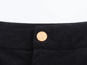 Vista macro dettagliata del tessuto a coste nero e del bottone dorato sulla vita dei pantaloni