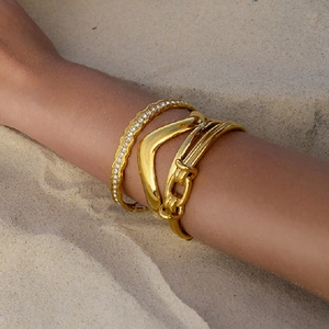 Elegantes Set aus goldfarbenen Edelstahl-Armbändern mit Kristallen auf Sandhintergrund