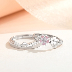 Makroaufnahme von Silber-Partnerringen mit rosa Kirschblüte und Bergrelief-Verzierung