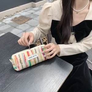 Detail of colorful knitted striped makeup bag with zipper closure and woven label