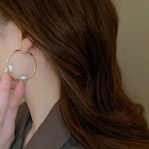 Close-up of a model wearing large gold-tone minimalist hoop earrings with glossy finish