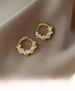 Detail shot of golden twisted hoop earrings with small white pearls on silk fabric
