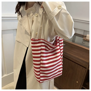Detail of red and white striped canvas tote bag worn with a beige trench coat