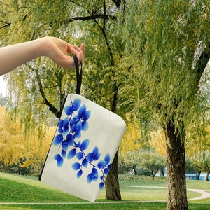 Pochette per trucco in tela con foglie blu e cinturino nero in un ambiente naturale