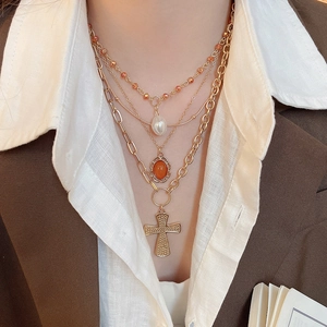 Detail of layered gold necklace with acrylic pearls, orange gemstone, and cross pendant