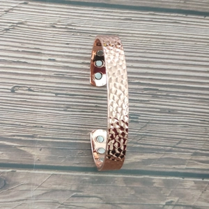 Macro shot of rose gold copper magnetic bracelet with hammered texture on wooden background