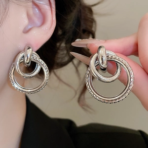 Détail de boucles d'oreilles créoles argentées texturées avec design à double cercle creux