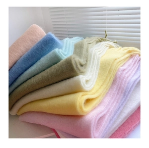 Close-up of stacked oversized plush scarves in various pastel colors with soft fiber texture