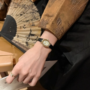Elegant vintage oval gold watch with diamonds and black leather strap on female wrist