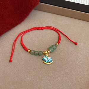 Dettaglio del bracciale rosso intrecciato con perle verdi e ciondolo cavallo a dondolo blu