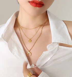 Detail of layered gold necklaces featuring sunburst medal and crescent moon charms