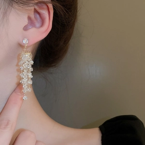 Vue détaillée de longues boucles d'oreilles dorées à pompons et cristaux clairs