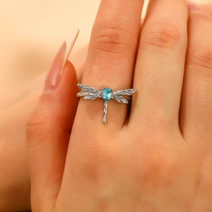 Close-up of silver dragonfly ring with blue teardrop gemstone on female finger