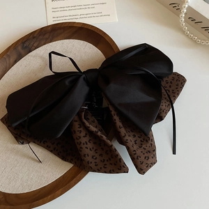 Chic leopard print bow hair clip on a wooden tray with elegant pearls and card